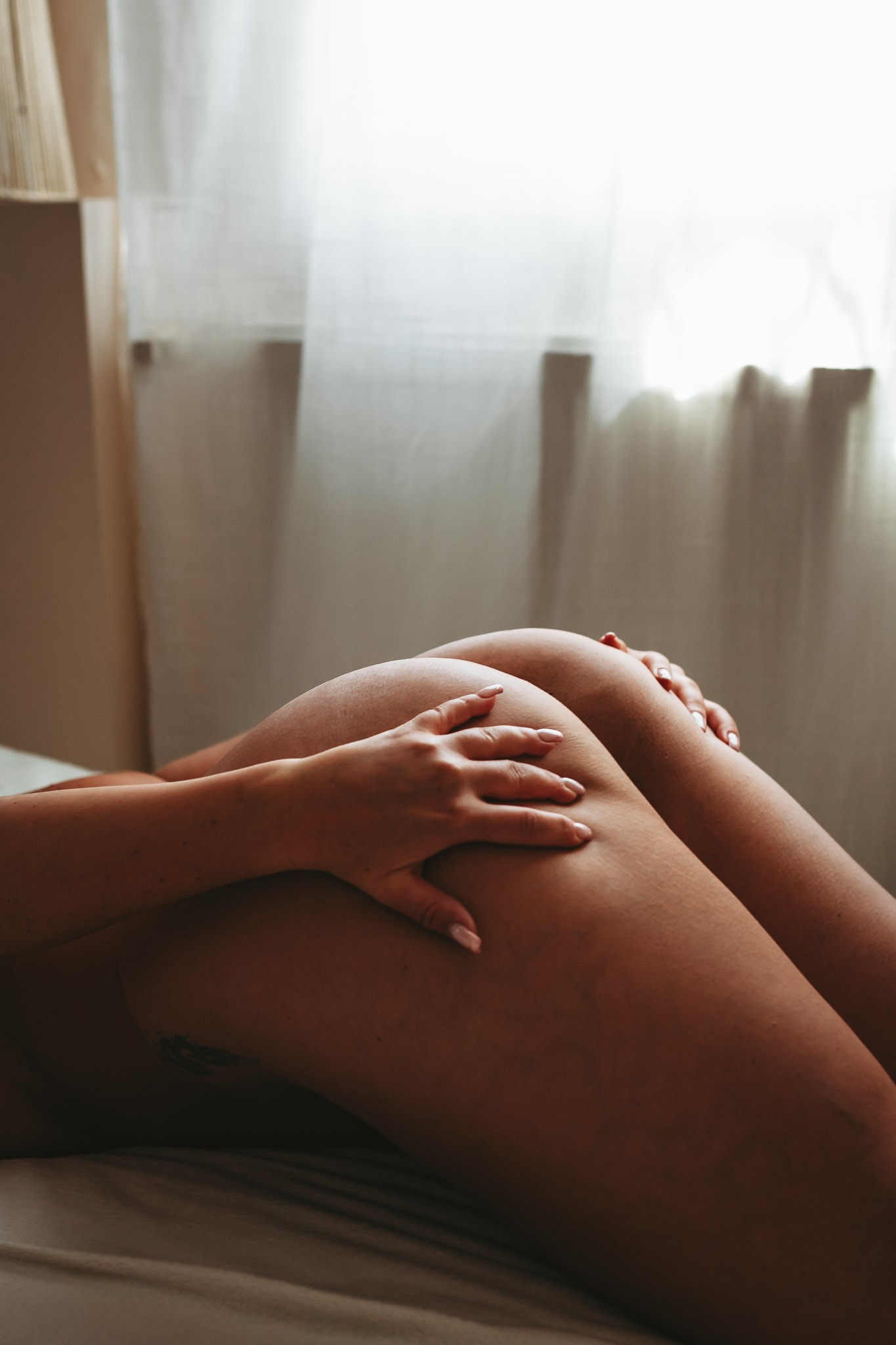 Közelkép egy nő combjairól és kezéről az ágyon fekve, természetes fényben – Boudoir Fotózás Budapesten